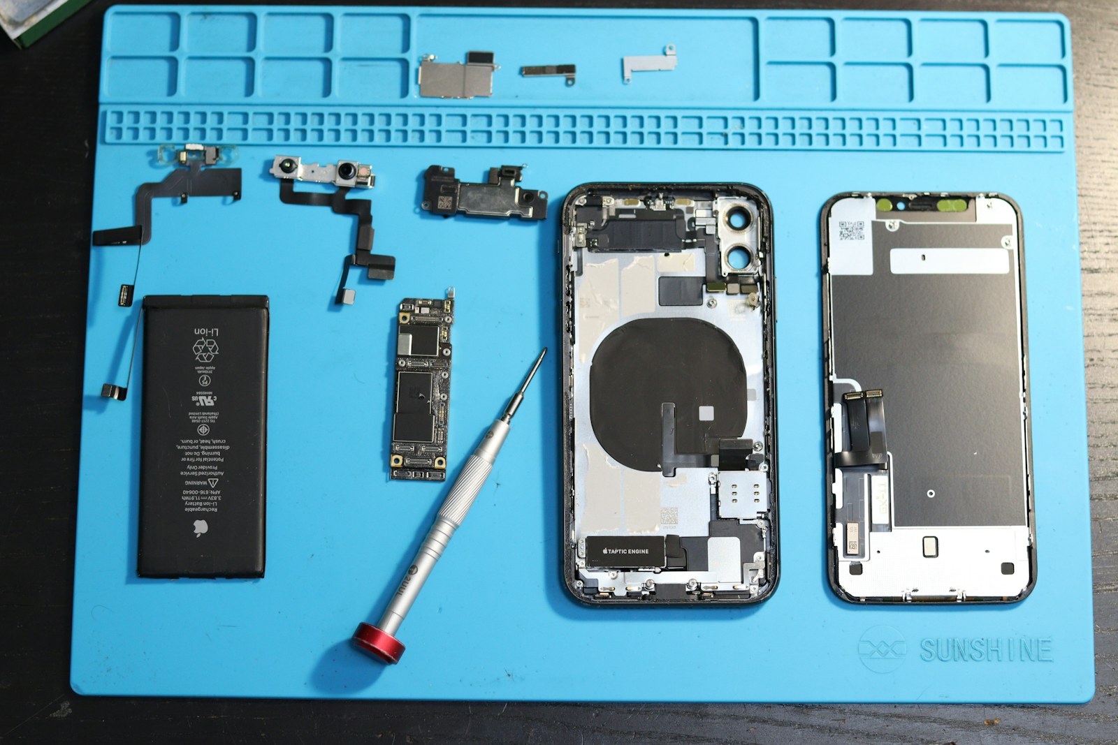Disassembled iPhone components and repair tools on a blue mat for checking used phone repair history